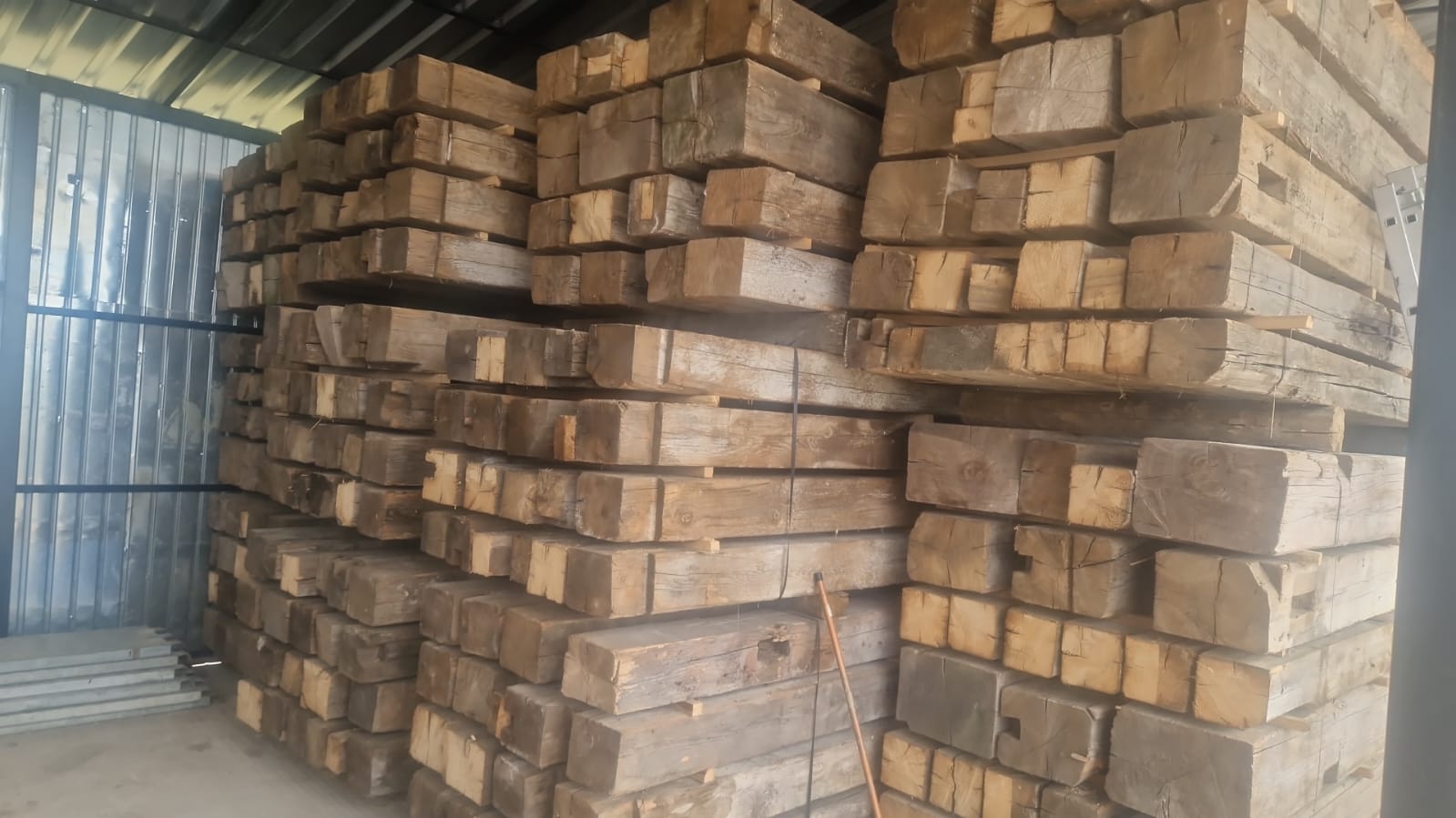 Reclaimed oak beams stacked outdoors, hand-hewn antique European timber with axe marks